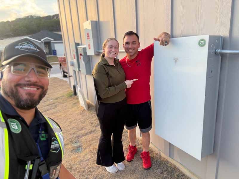 Three people smiling beside a white utility box outside a building, one taking a selfie.