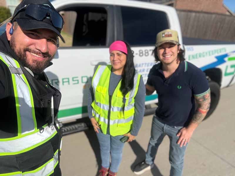 Three people in safety vests posing beside a work truck outdoors.