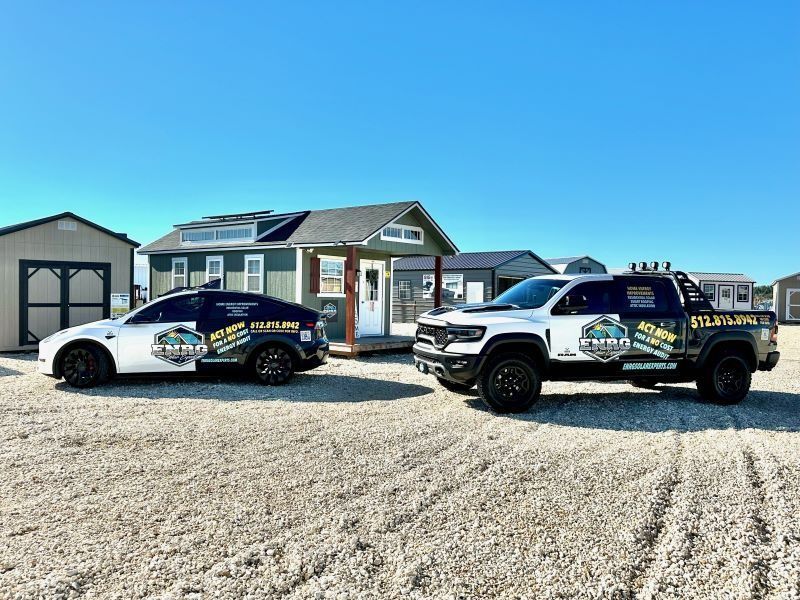 Two branded service cars parked on a gravel lot in front of a small house under a clear blue sky