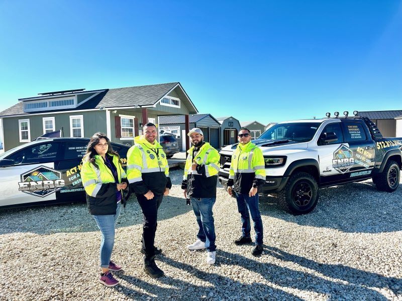 Four people in safety vests stand outside near a house and a white lifted pickup truck.