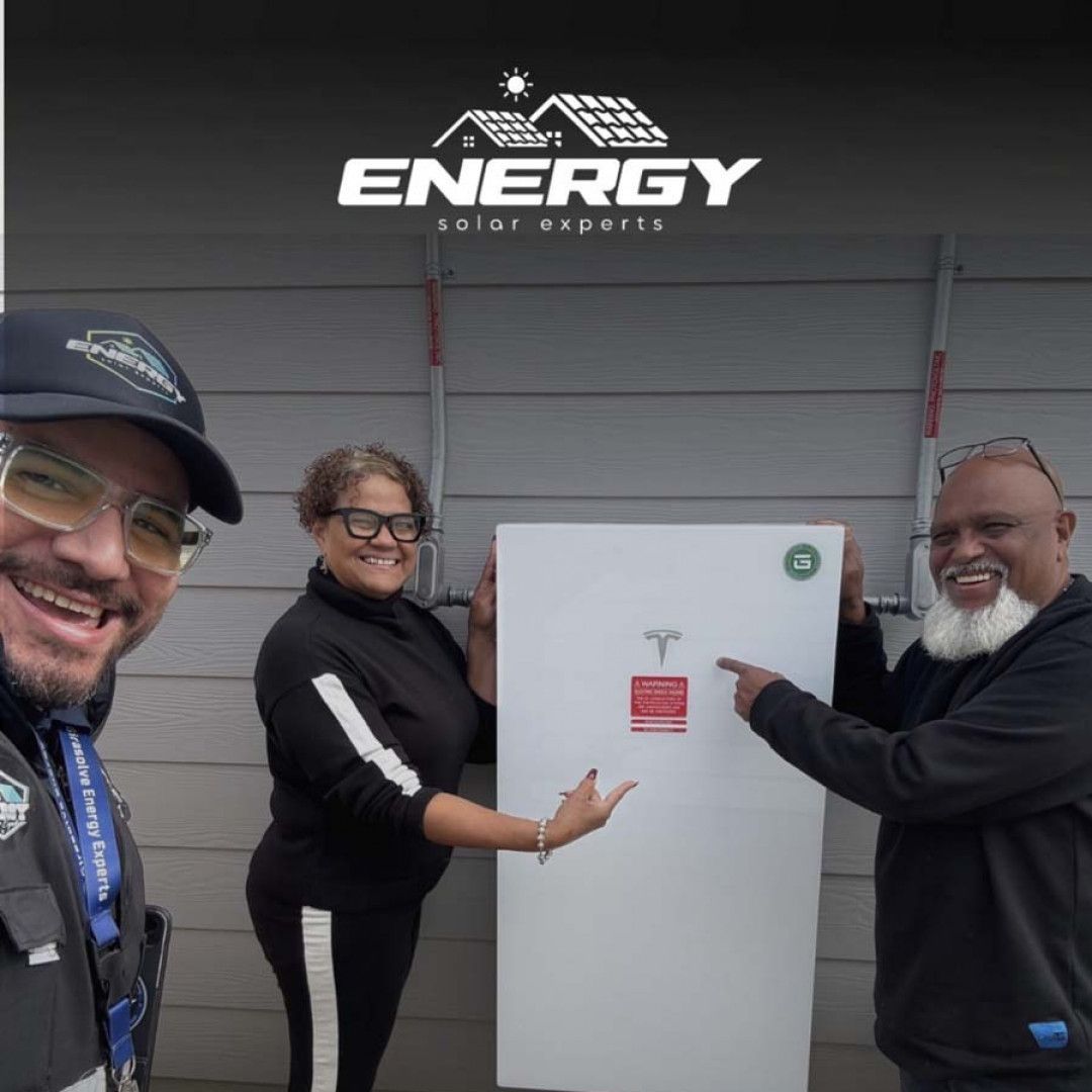 Three people smile and point at a white refrigerator in front of an ENERGY Edge Experts sign.