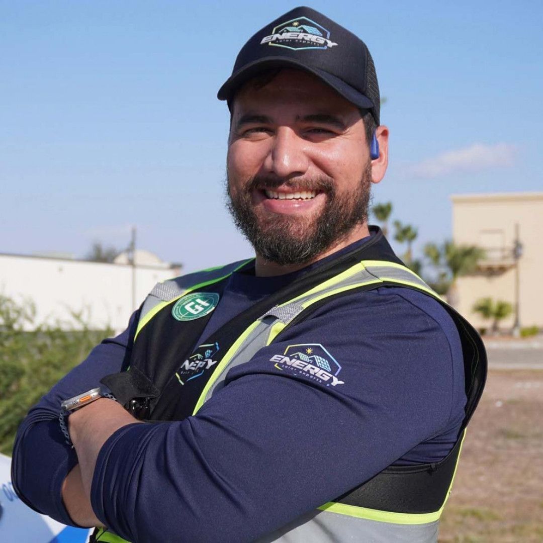 Smiling worker in navy uniform and cap with safety vest, standing outdoors on a sunny day.