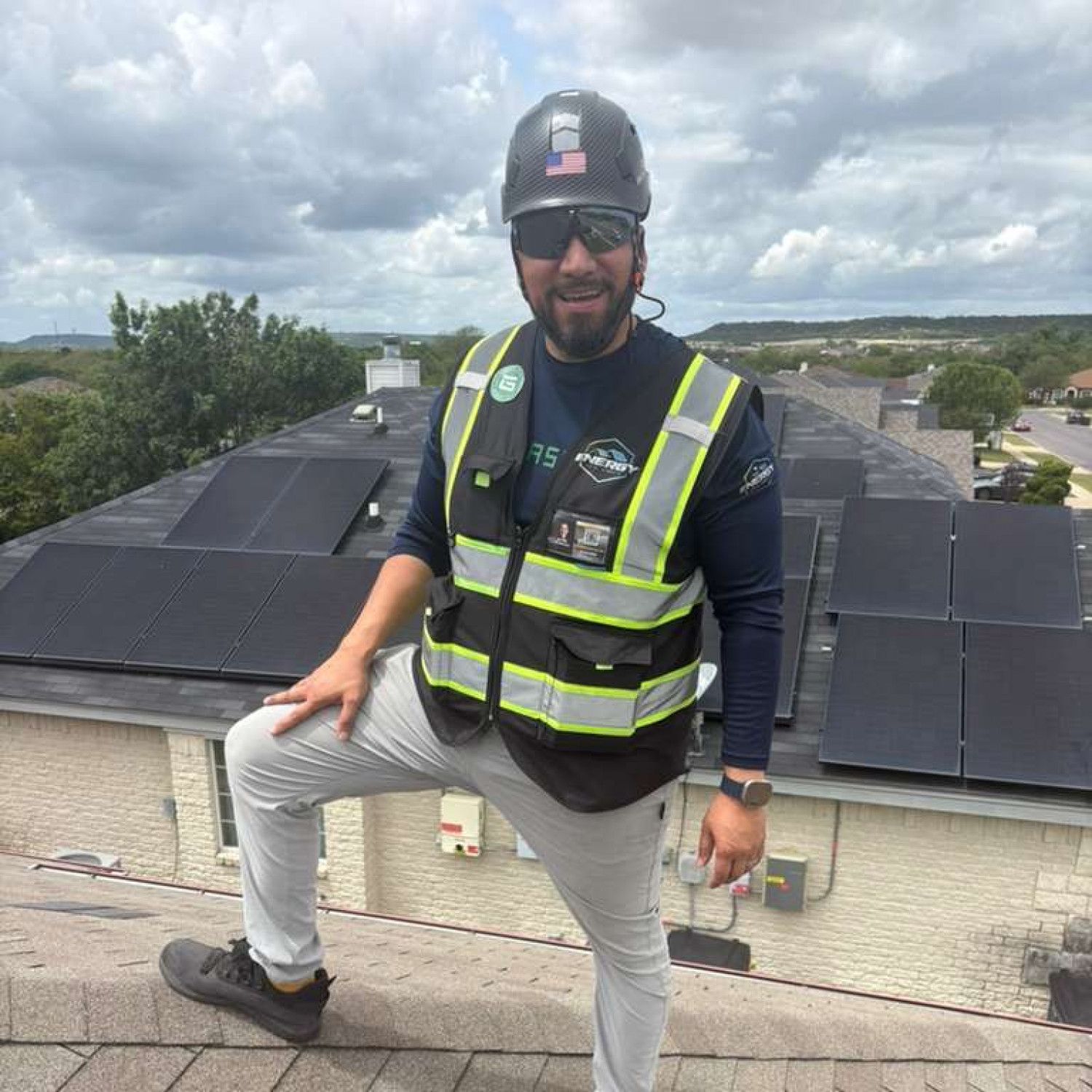Worker in safety vest and hard hat posing on a rooftop with solar panels under a cloudy sky