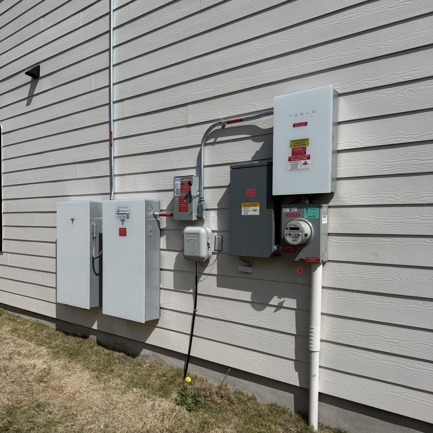 Outdoor utility meters and electrical panels mounted on a white building wall.