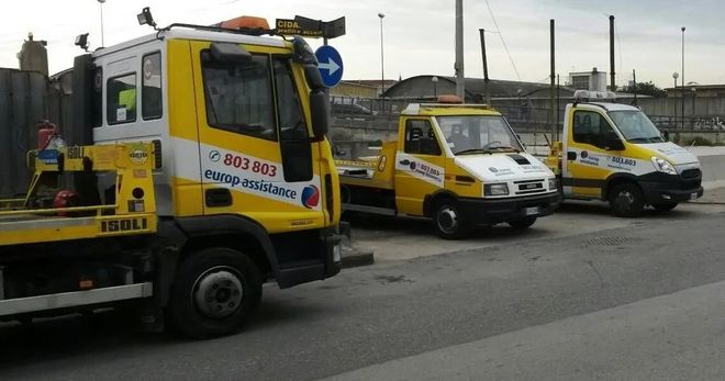 In una giornata nuvolosa, tre carri attrezzi gialli e bianchi erano parcheggiati in fila in un parcheggio all'aperto.