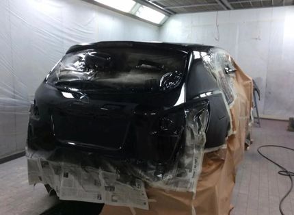 Un'auto nera sottoposta a verniciatura professionale in una cabina di verniciatura per auto, protetta da nastro adesivo e carta protettiva.