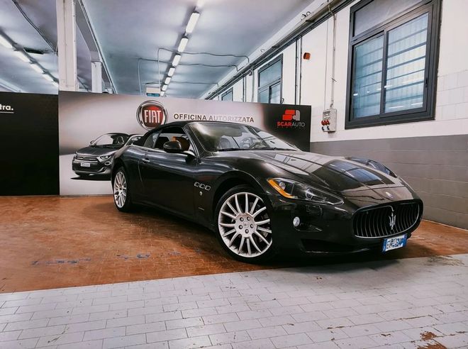 Una Maserati sportiva di colore scuro parcheggiata all'interno di un garage, sul pavimento, di fronte a una parete con il marchio Fiat.