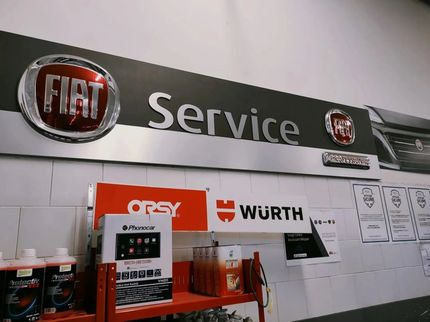 Cartelli informativi del servizio assistenza Fiat su una parete sopra degli scaffali con il marchio Wurth e vari prodotti per la manutenzione automobilistica.