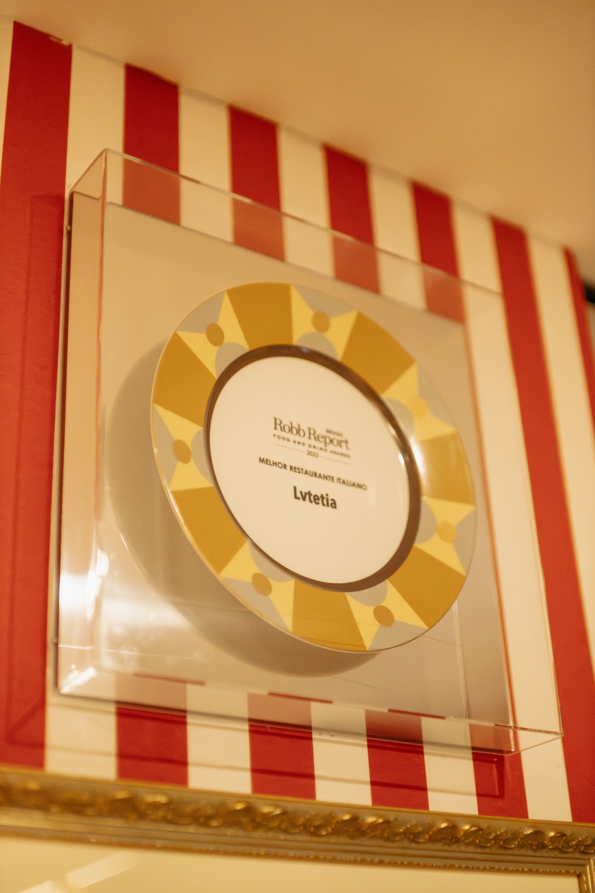 Placa emoldurada com borda amarela de bolinhas em uma parede listrada em vermelho e branco.
