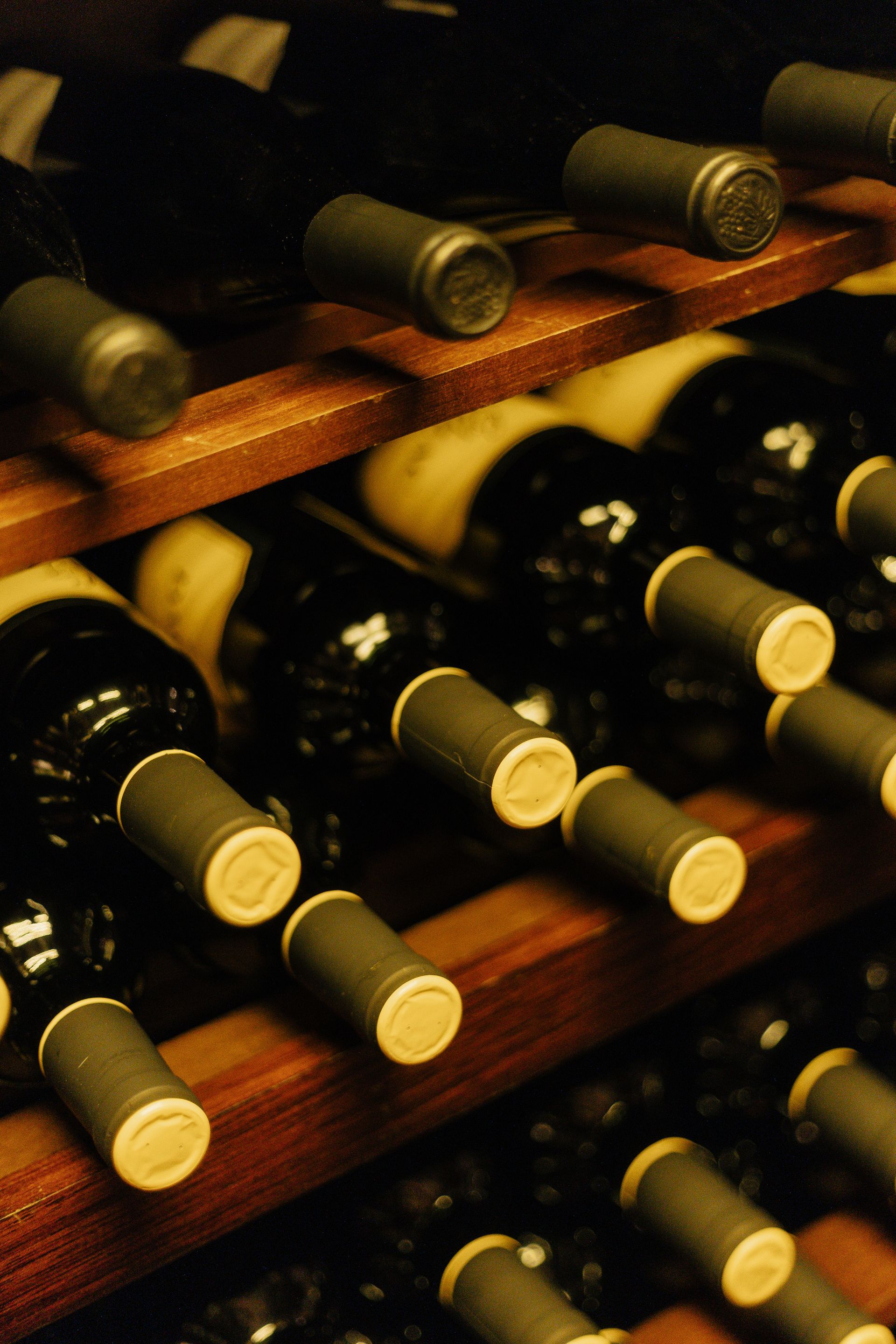Garrafas de vinho armazenadas em prateleiras de madeira em uma adega com iluminação suave.