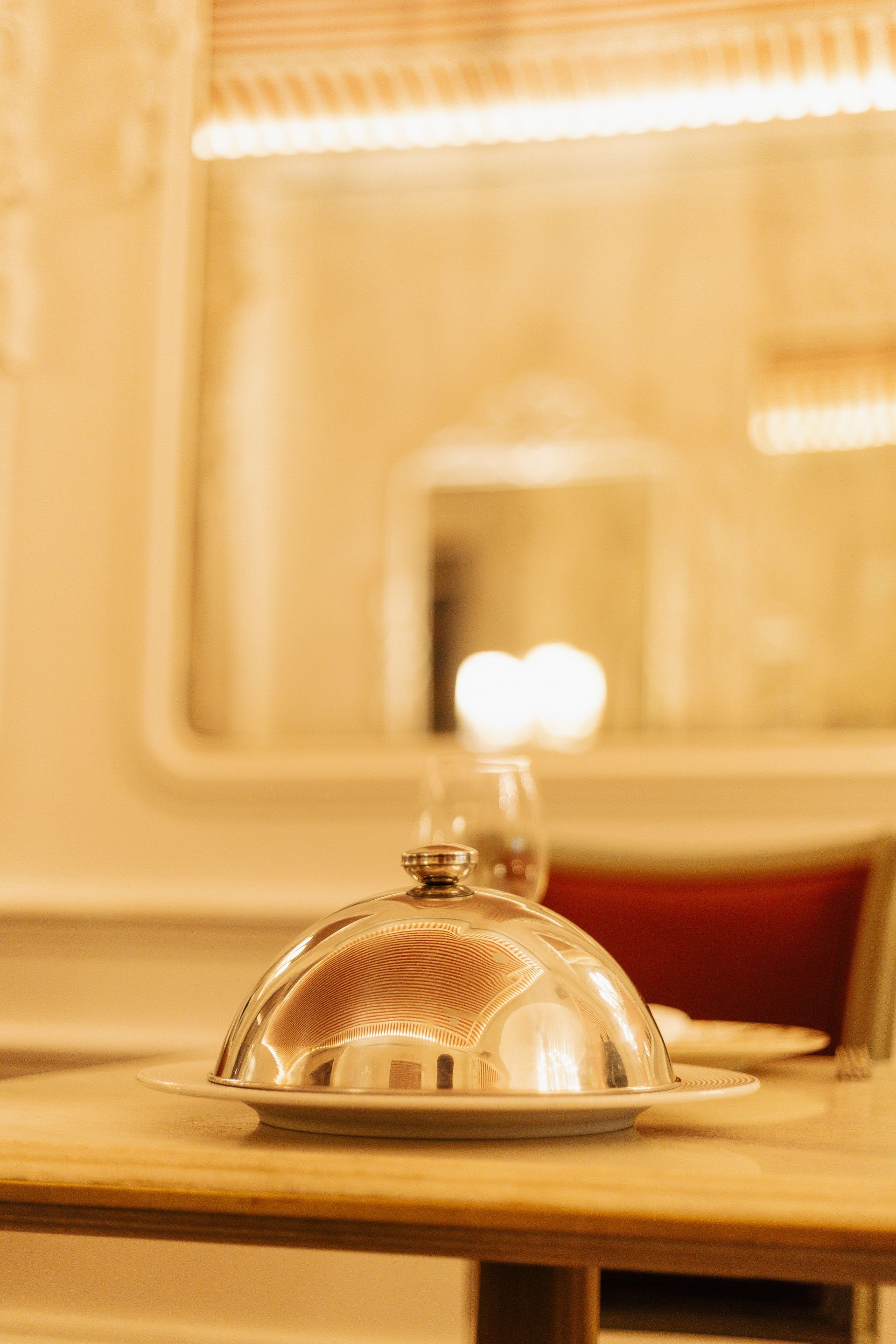Cloche de prata sobre uma mesa de restaurante em uma sala de jantar com iluminação aconchegante.