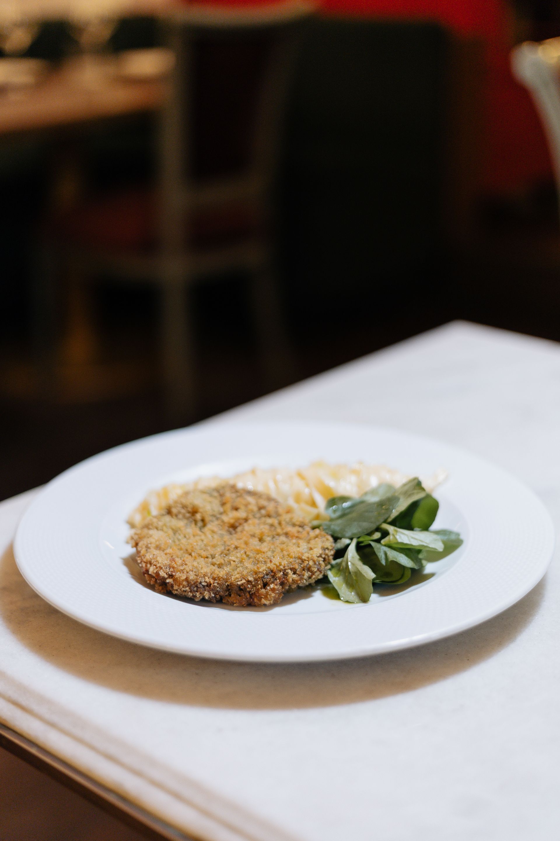 Prato empanado com verduras em um prato branco em uma mesa de restaurante.