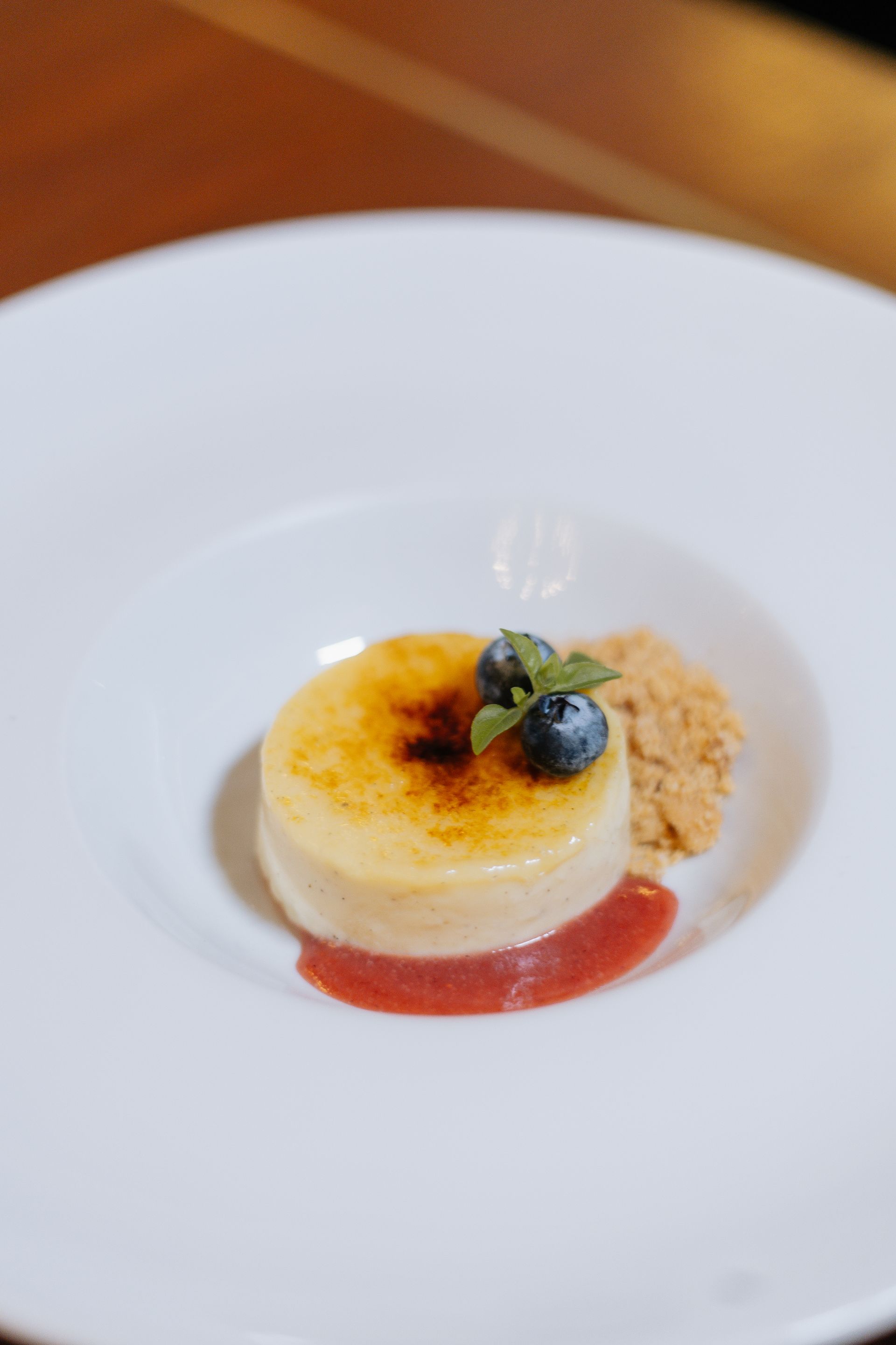Pequena sobremesa de crème brûlée com frutas vermelhas e calda em um prato branco.