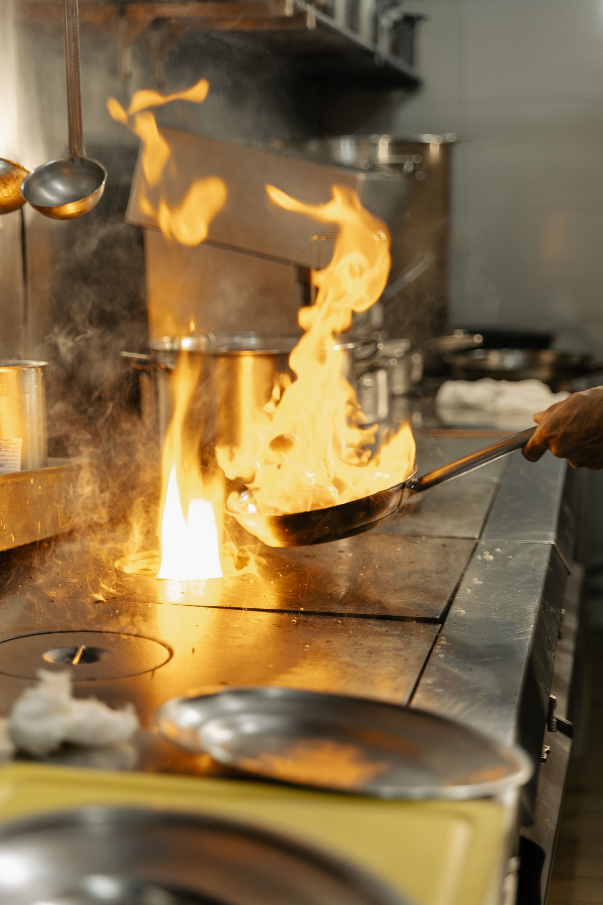 Chef prepara comida em chamas em uma cozinha com uma wok em fogo alto.