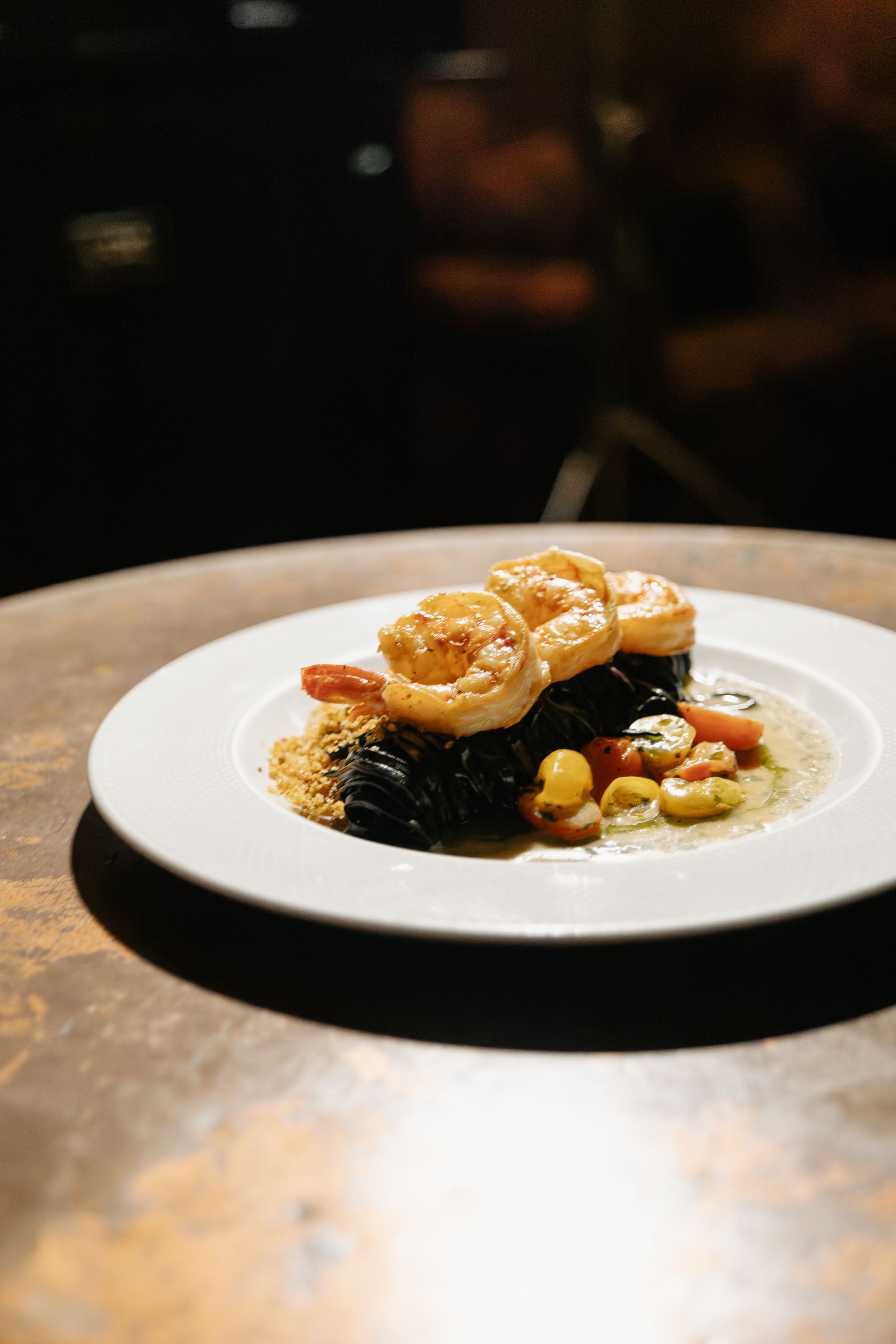 Prato gourmet com molho e legumes disposto em uma mesa de restaurante, suavemente iluminado contra um fundo escuro.
