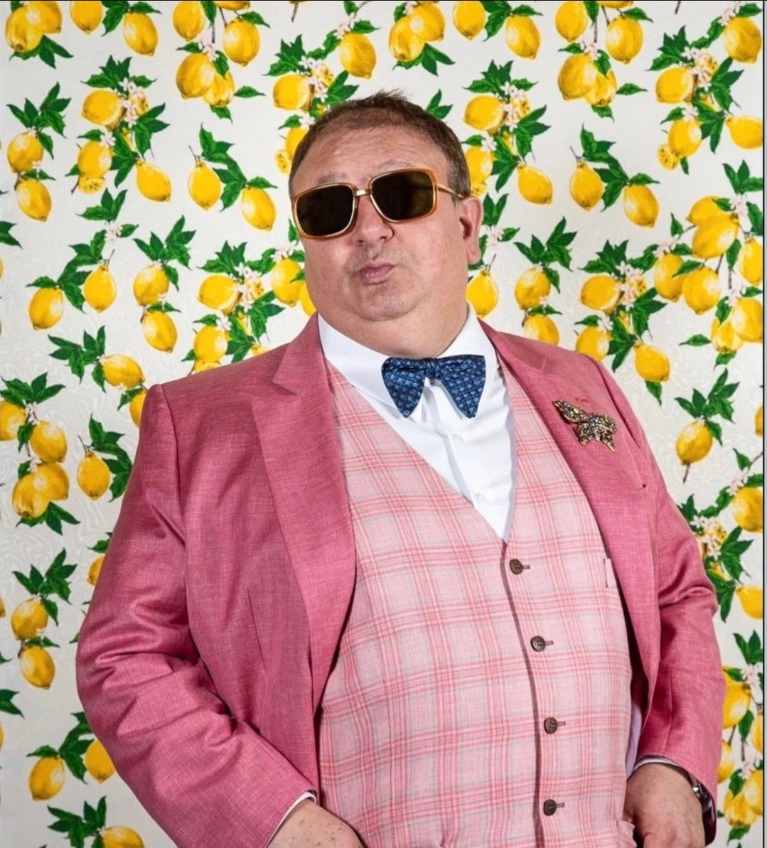 Homem de terno rosa e óculos escuros posando em frente a um fundo com estampa de limão.
