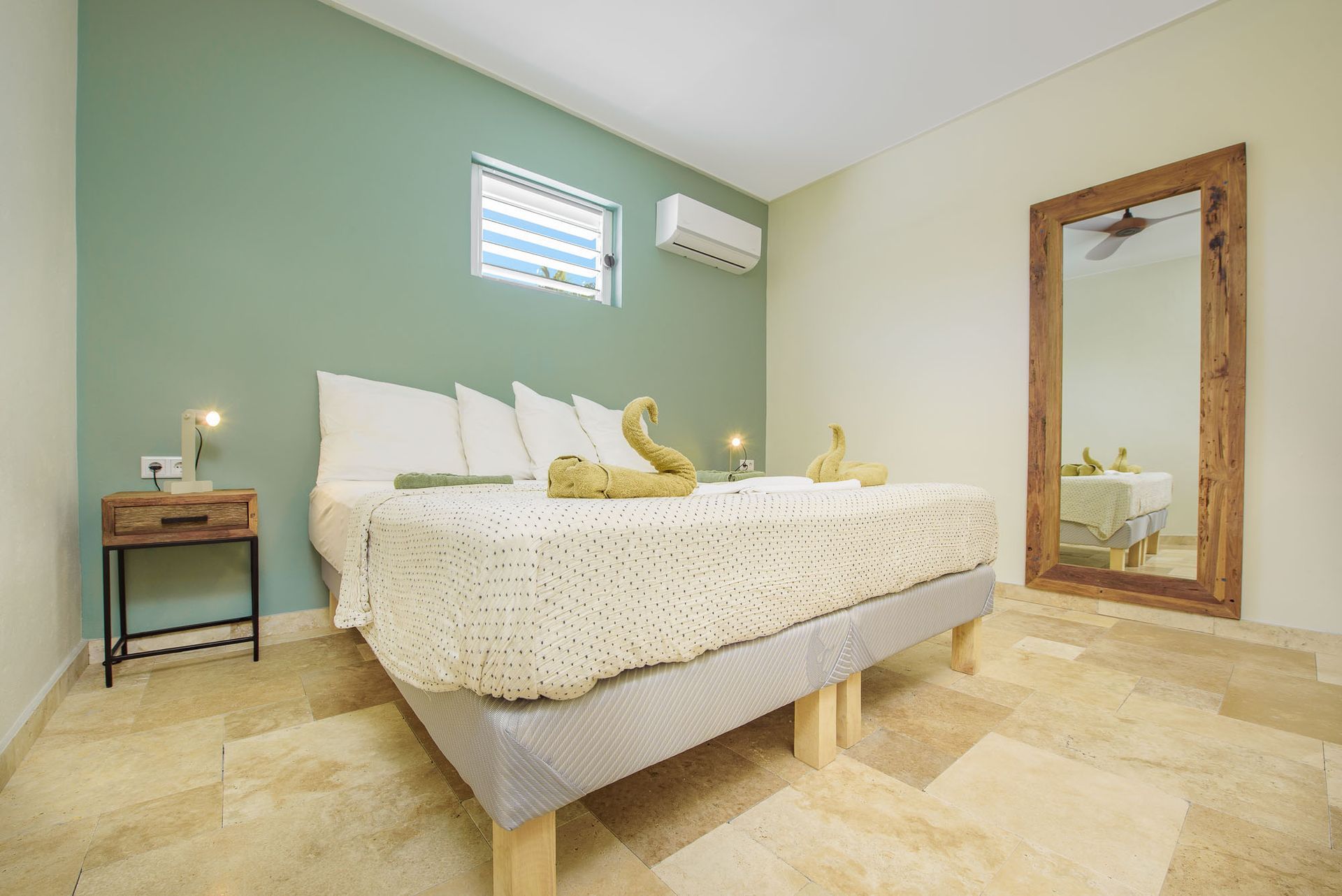 Bedroom with a bed, large mirror, wooden nightstand, and sage green accent wall.