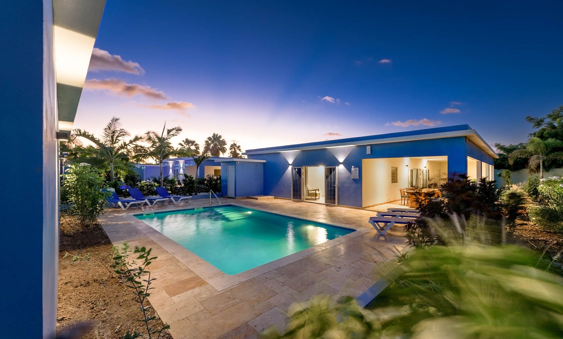 Blue house with pool at dusk; pool has turquoise water.
