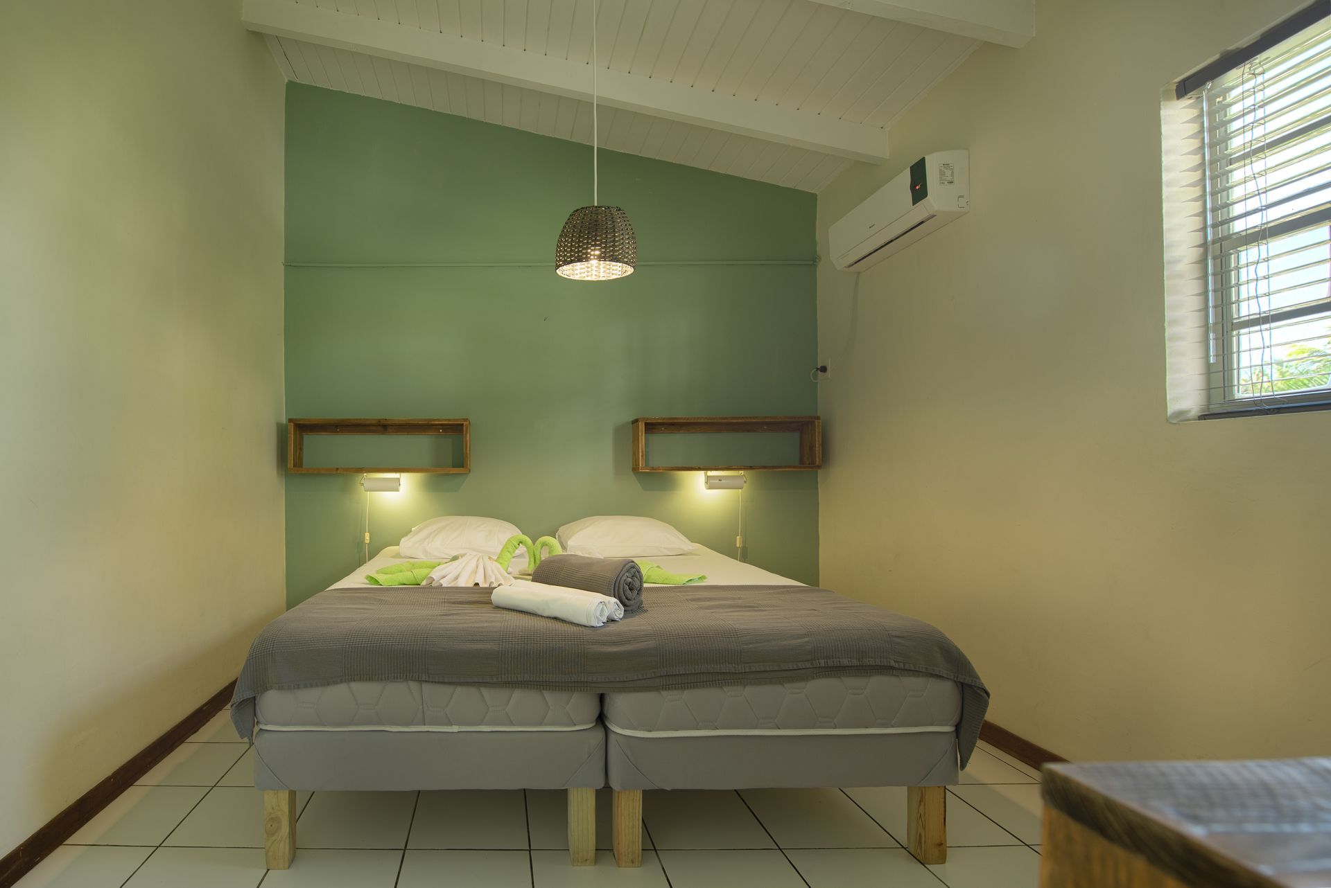 Bedroom with double bed, green accent wall, wooden shelves, window, and air conditioner.