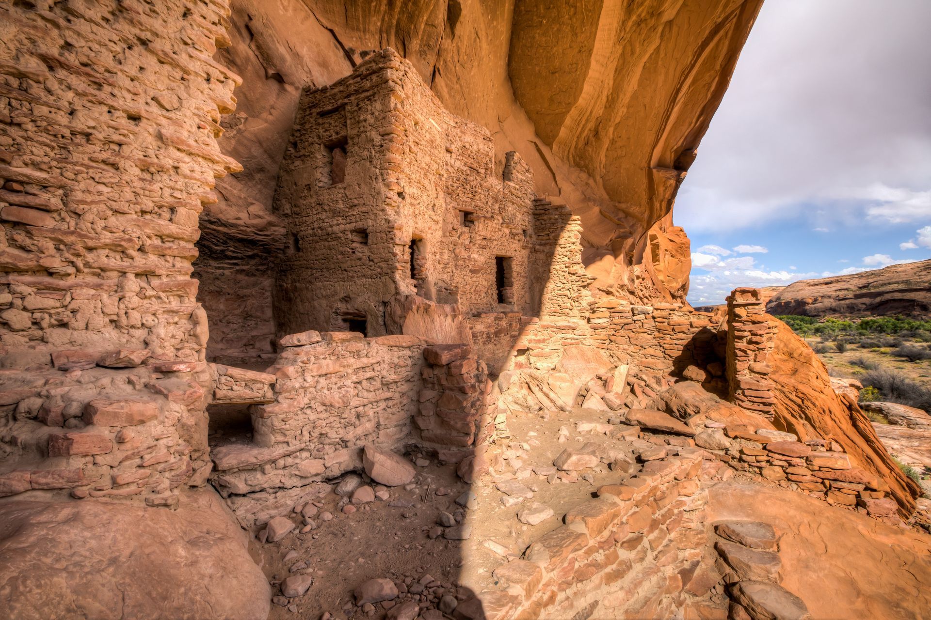 Ancient Puebloan structures built into a red rock cliff overseeing a valley