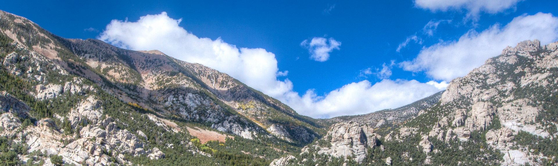 Mountains with granite and green trees against a blue sky with white clouds.