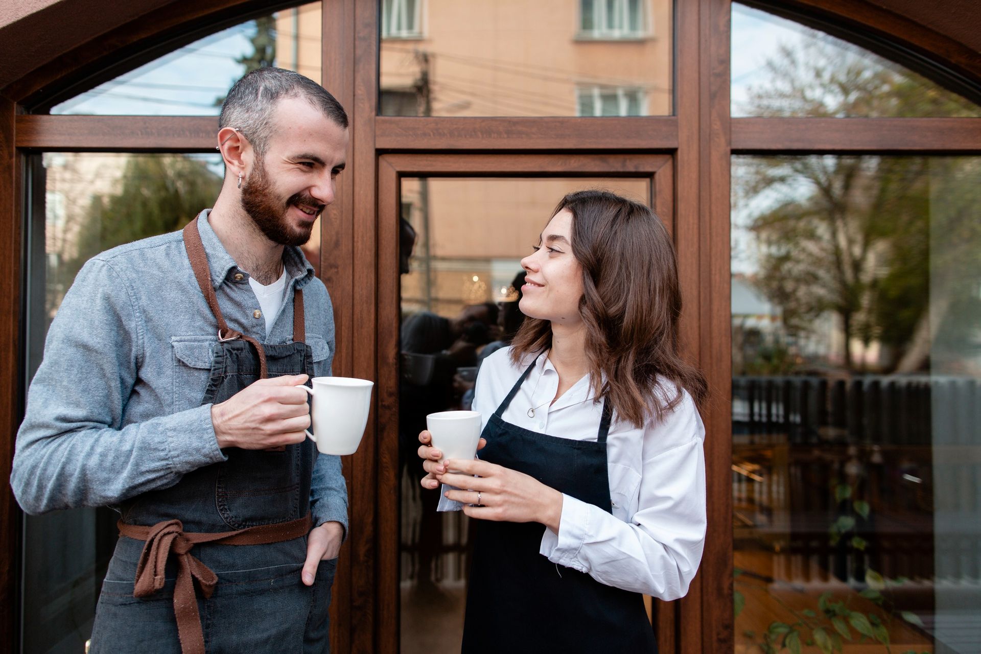 Two people chatting with coffee cups outside a storefront entrance