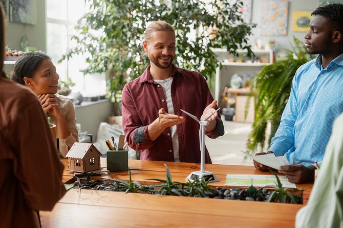 Three people discussing a model home at a table with plants and house miniatures