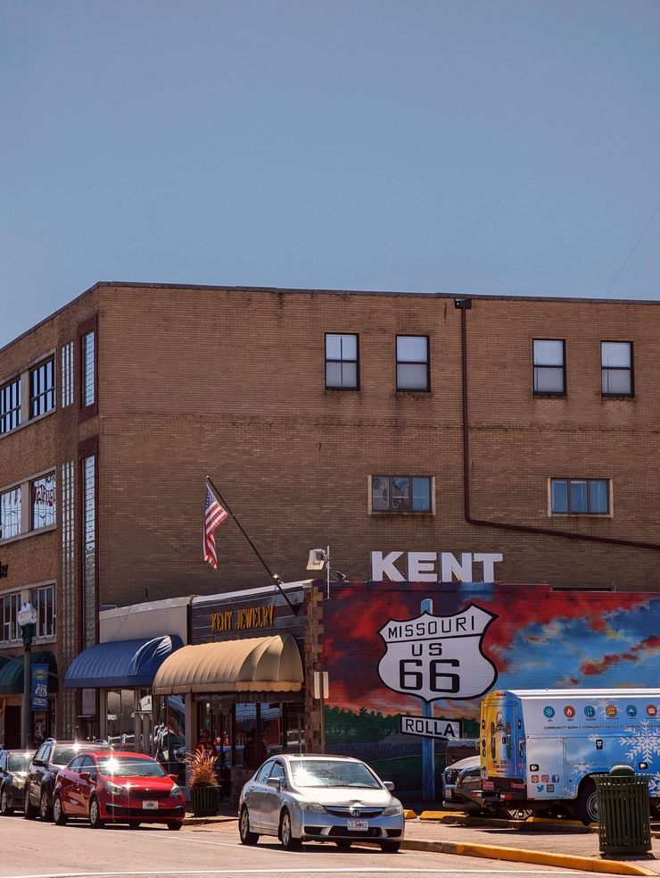 Street scene with a brick building, Route 66 mural, and parked cars under a clear sky.