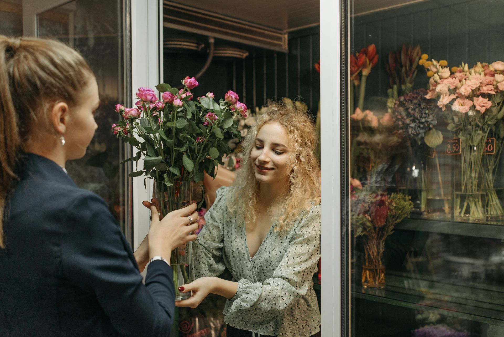 Woman handing a bouquet to a smiling florist at a flower shop window