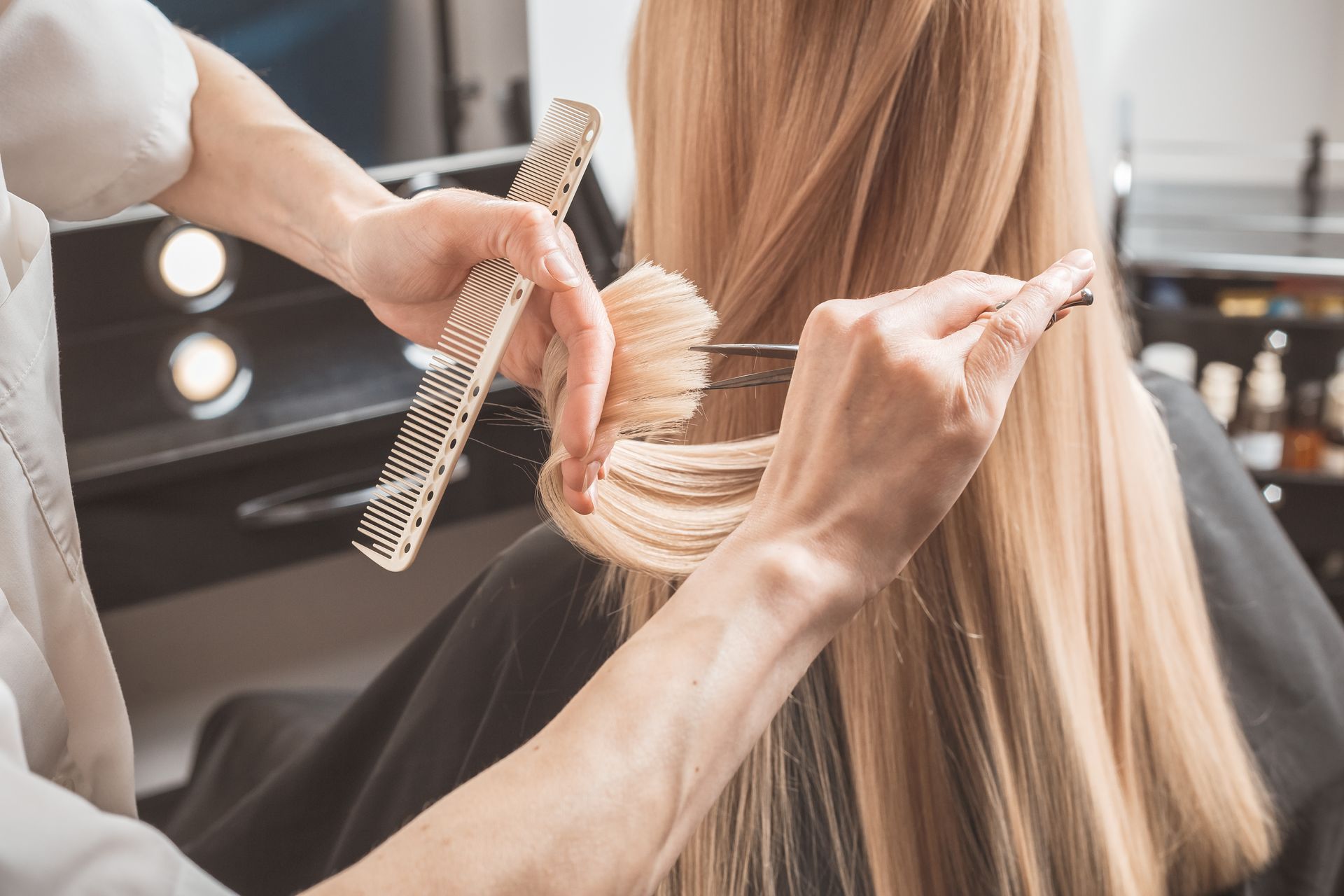 Stylist cutting long blonde hair with scissors and a comb in a salon. Stylist cutting long blonde hair with scissors and a comb in a salon.