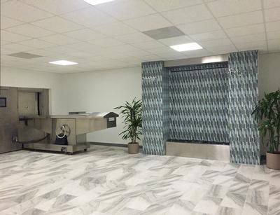 A mortuary room with stainless steel equipment, tiled wall with fountain, potted plants, and marble floors.