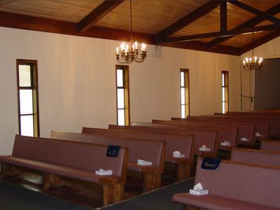 Empty chapel interior with pews, tall windows, chandeliers, and wooden beams.