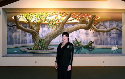 Woman in black standing before a large mural of a tree, pond, and swan with fall foliage.