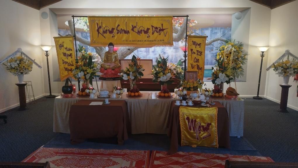 Altar with Buddha statue, flowers, and offerings in a temple or shrine setting.