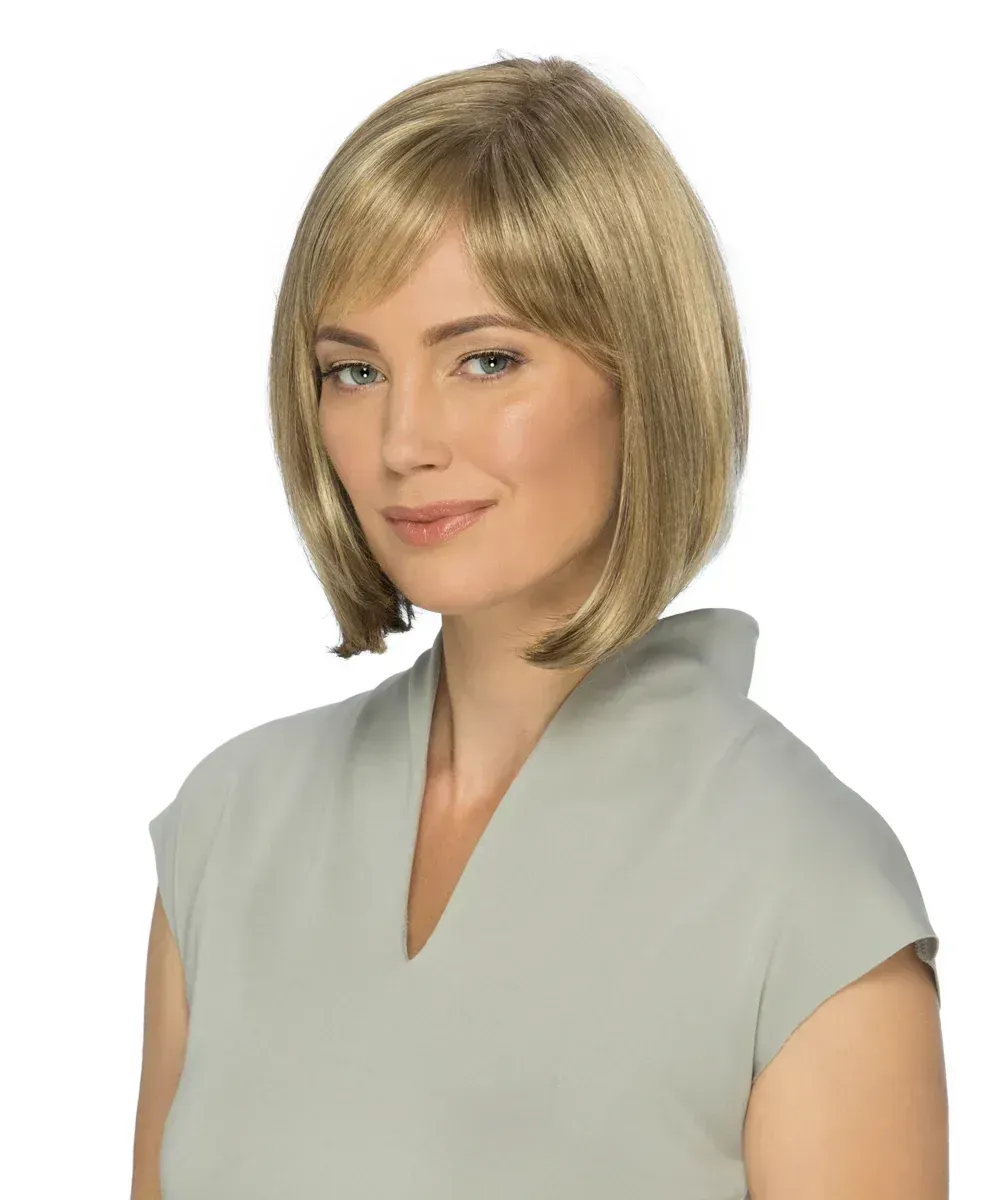 A woman wearing a wig and a grey shirt is standing in front of a white background.