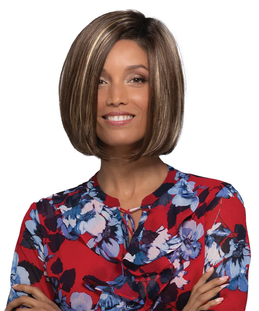 Woman with short brown bob and blonde highlights, wearing a red floral top, smiling with arms crossed.