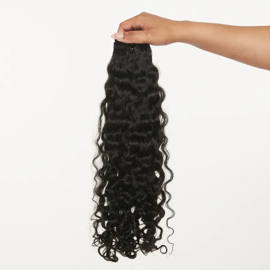 Hand holding a bundle of long, black, curly hair extensions against a white background.