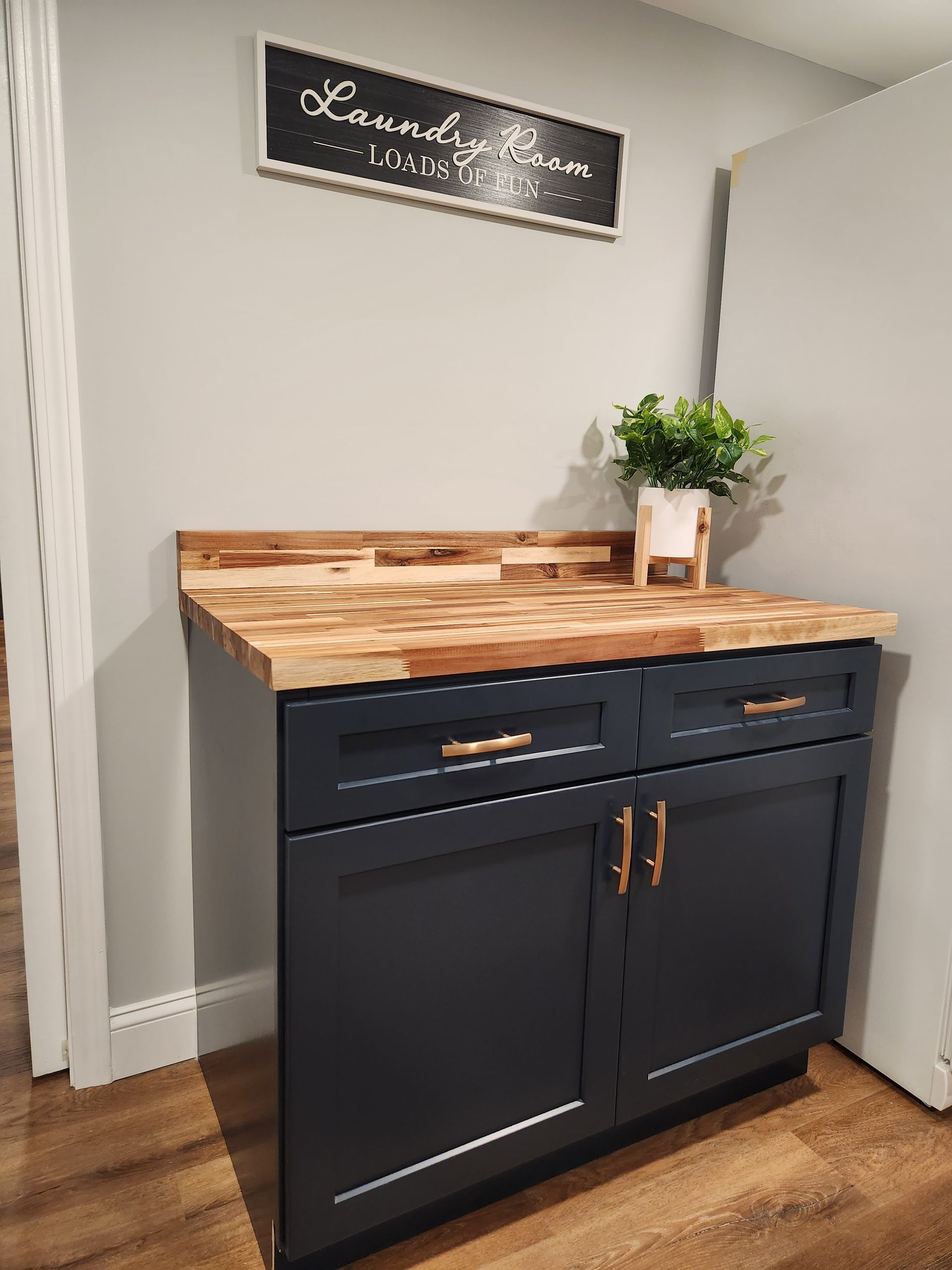 A laundry room with a wooden counter top and black cabinets.