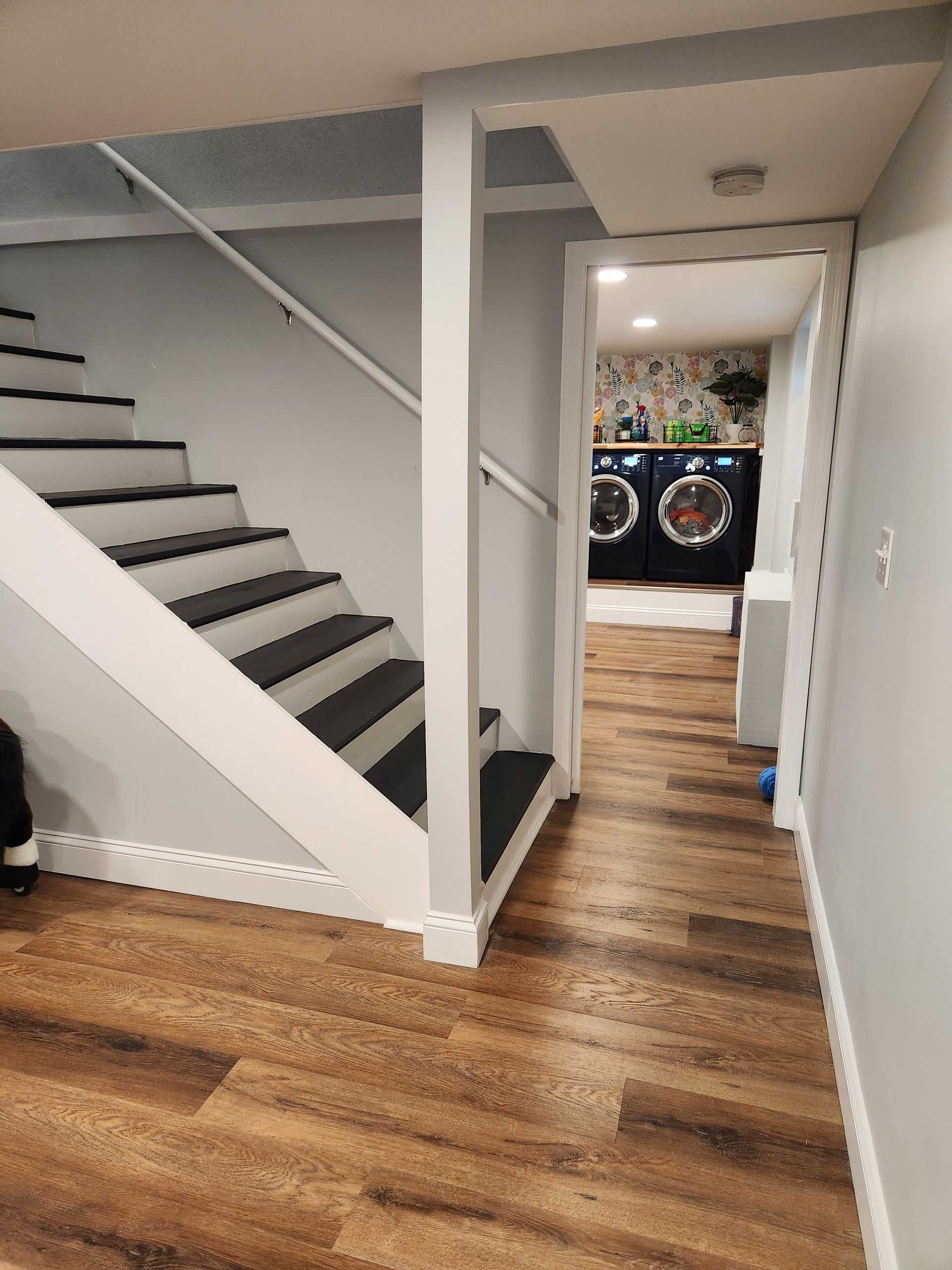 A basement with hardwood floors and stairs leading up to a laundry room.