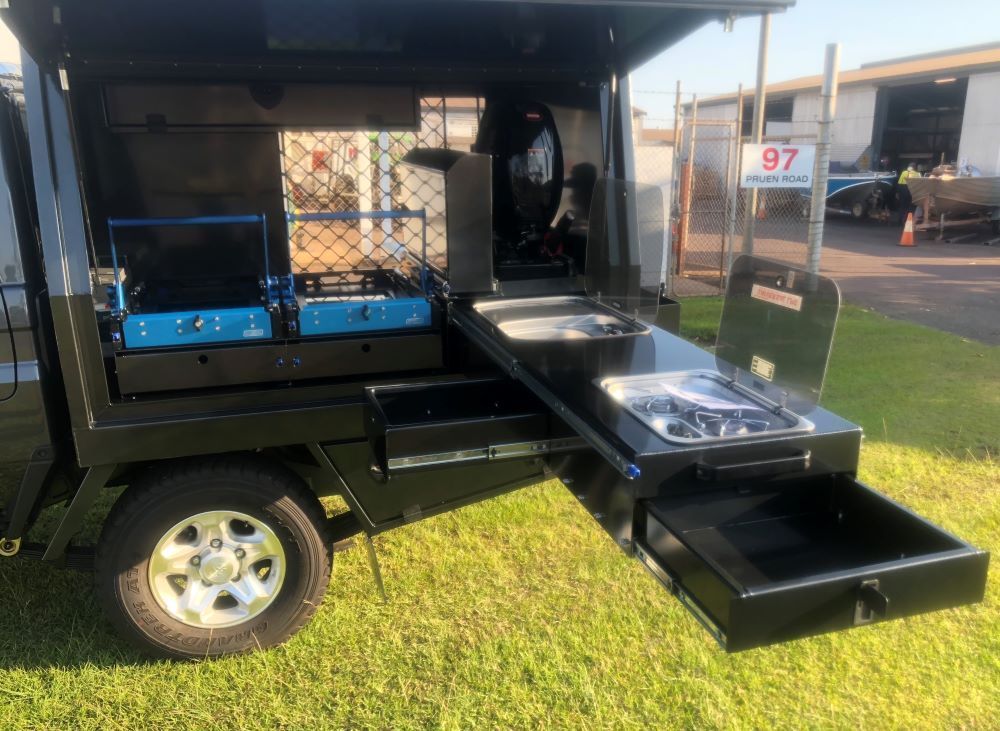 A Black Pickup Truck Featuring a Canopy and Built-in Drawers is Stationed in a Grass Field — Allycraft Modifications in Berrimah, NT