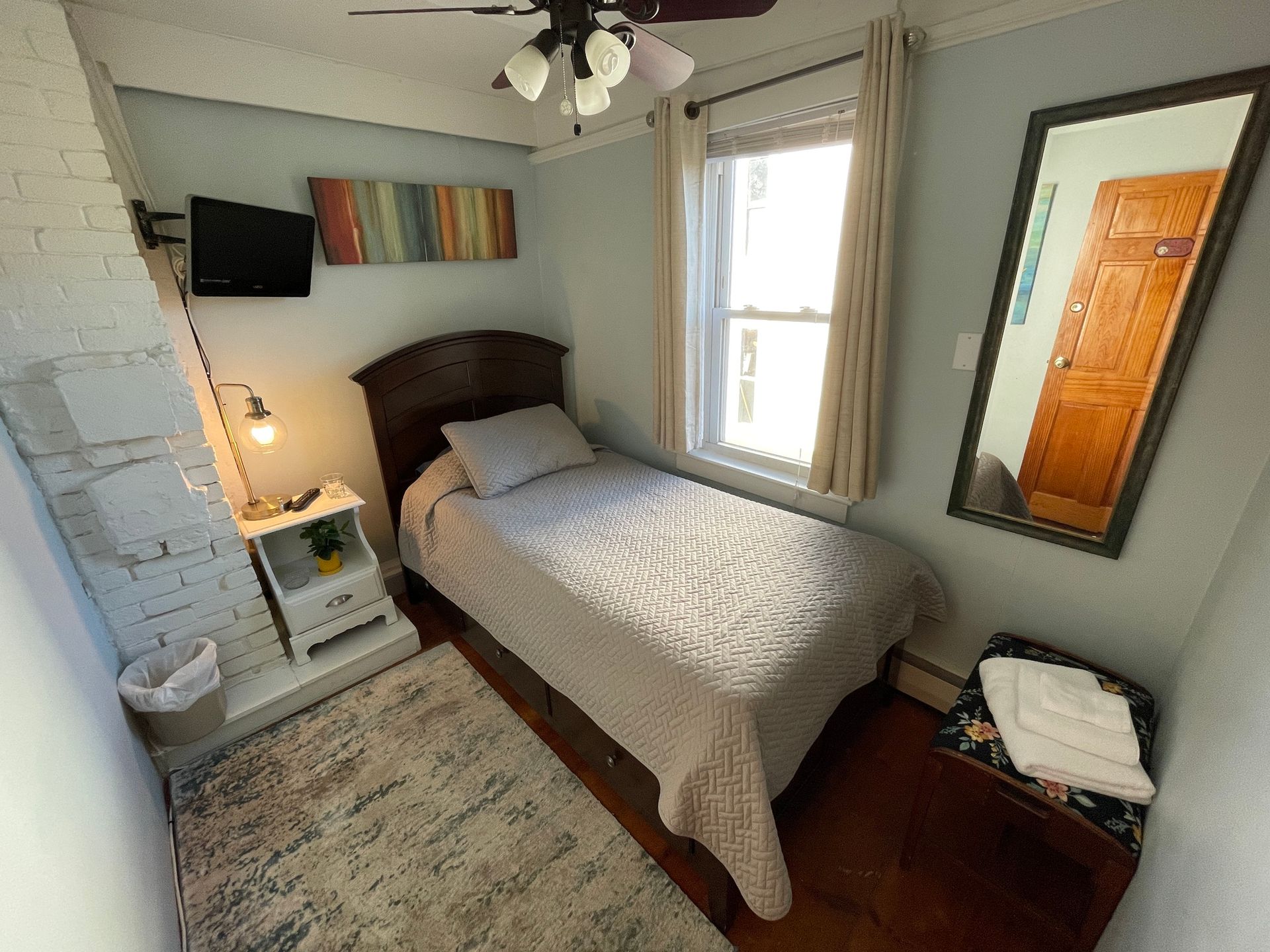 A small bedroom with a single bed and a mirror.