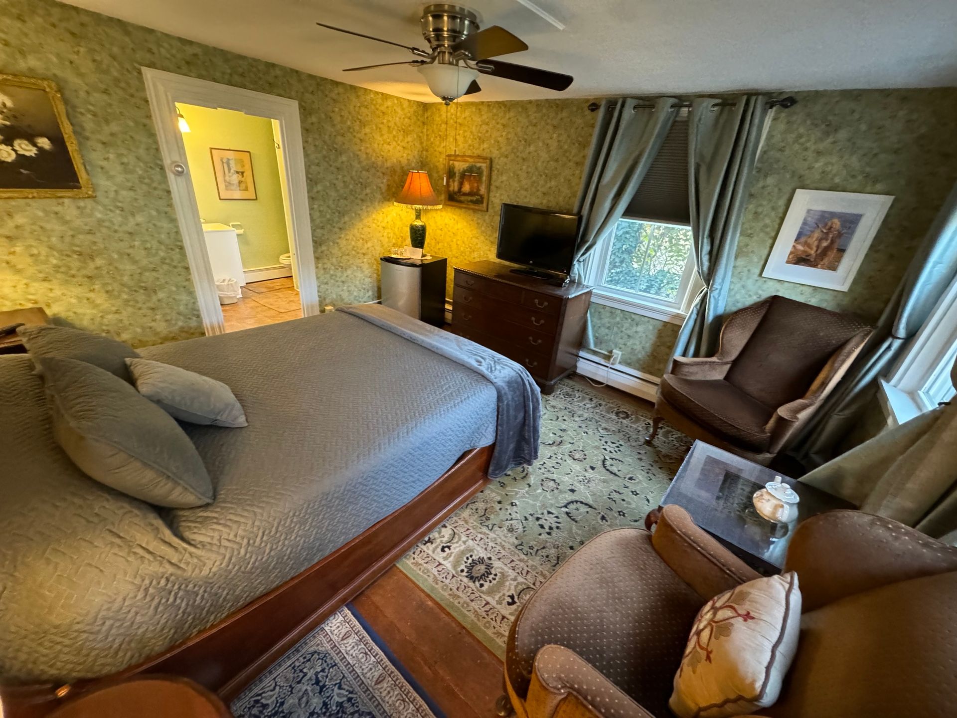 A bedroom with a bed , chairs , a television and a ceiling fan.