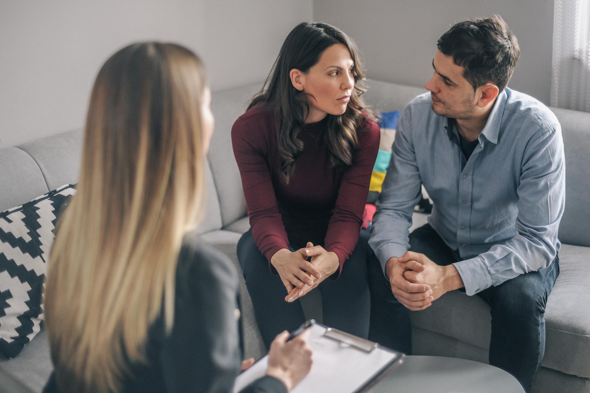 Three people in a counseling session, seated on a couch and talking with a therapist taking notes.