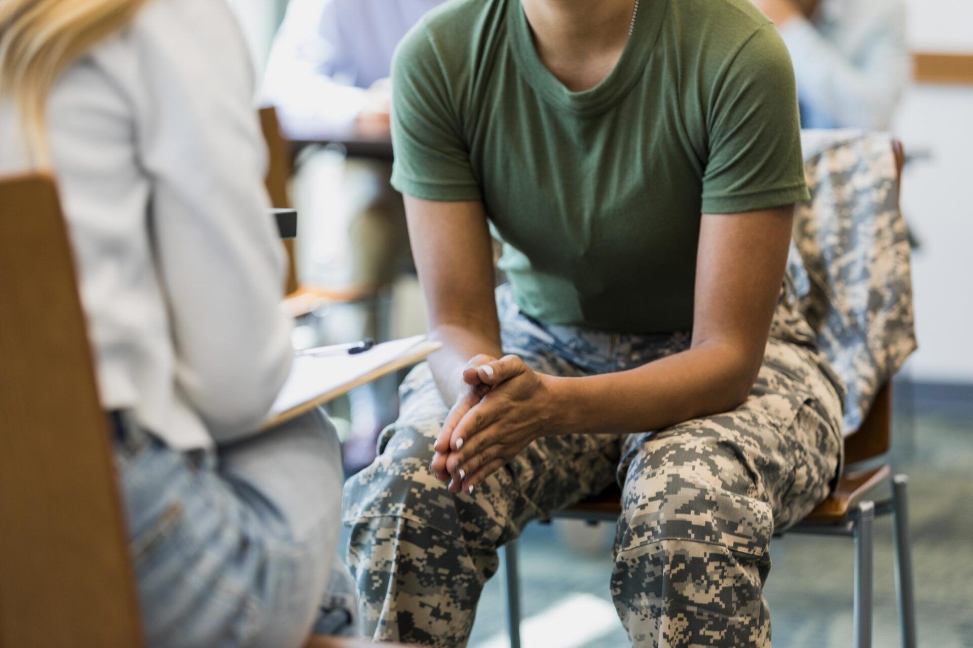 Person seated in camouflage pants, talking with a clinician in a white coat in a medical office
