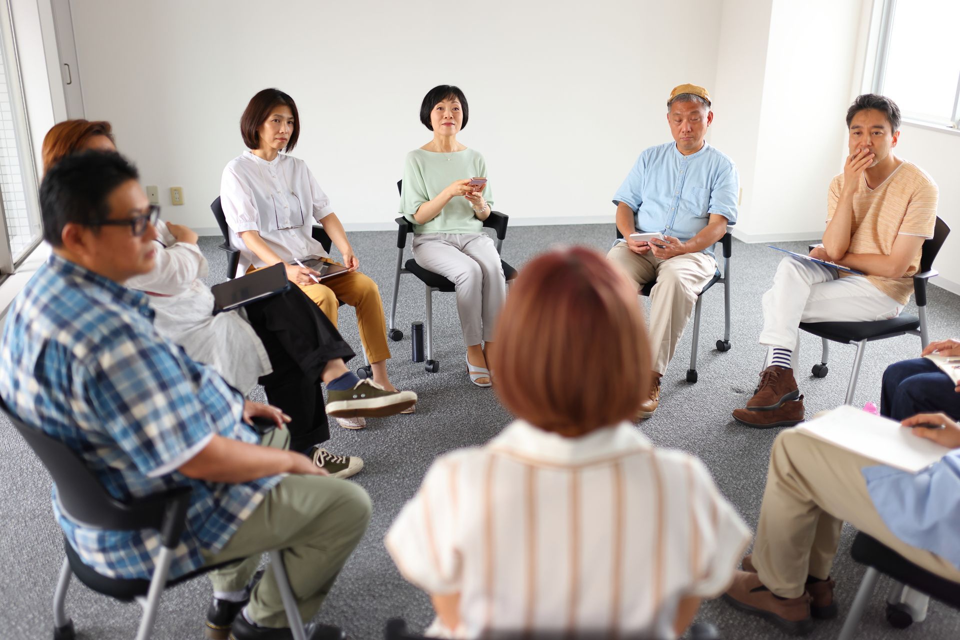 Small group seated in a bright room, holding a discussion circle with papers and clipboards.