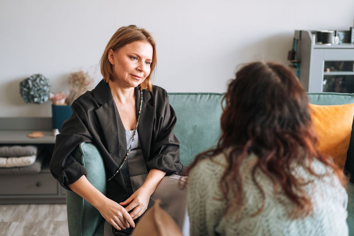 Two people talking on a couch in a cozy living room, one facing the other and listening attentively.