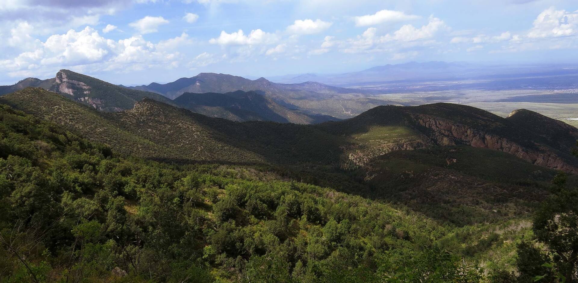 Mountain landscape with green hills, rocky ridges, and a cloudy blue sky