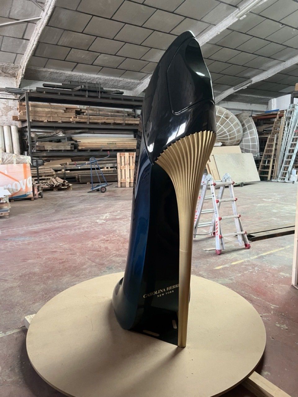 Un gran zapato negro con tacón dorado está sobre una mesa en un almacén.