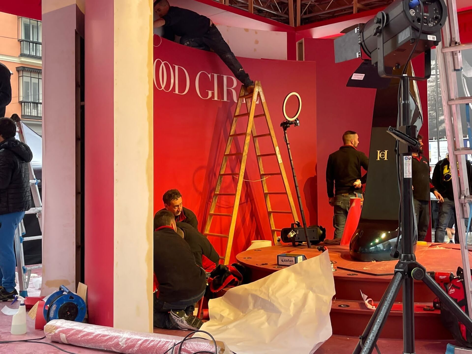 Un grupo de personas está trabajando en un escenario frente a una pared roja.