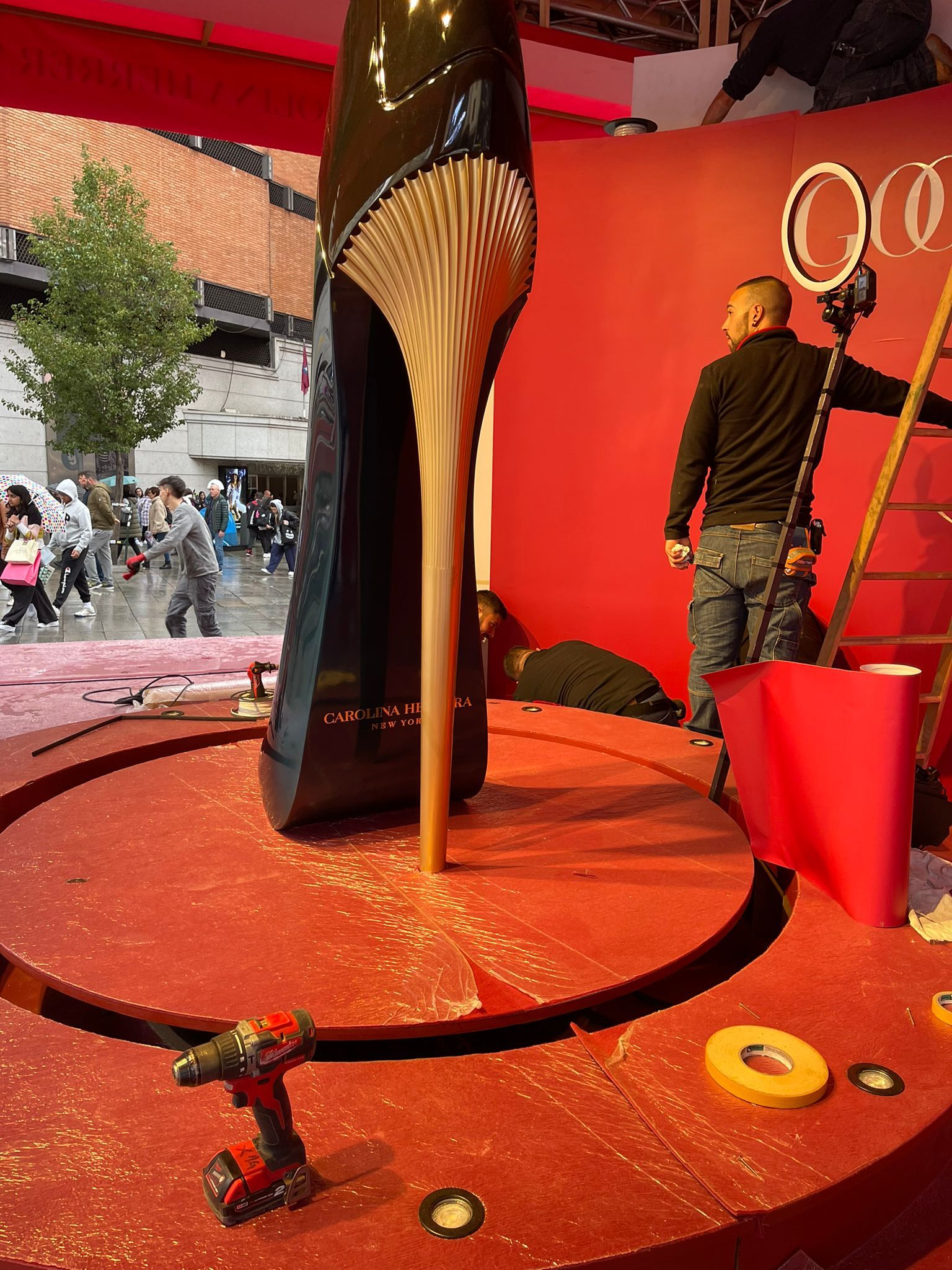 Un hombre está parado junto a un zapato grande sobre una superficie roja.